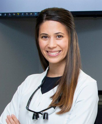 The image shows a smiling woman wearing a white lab coat, standing in front of a screen displaying a presentation.