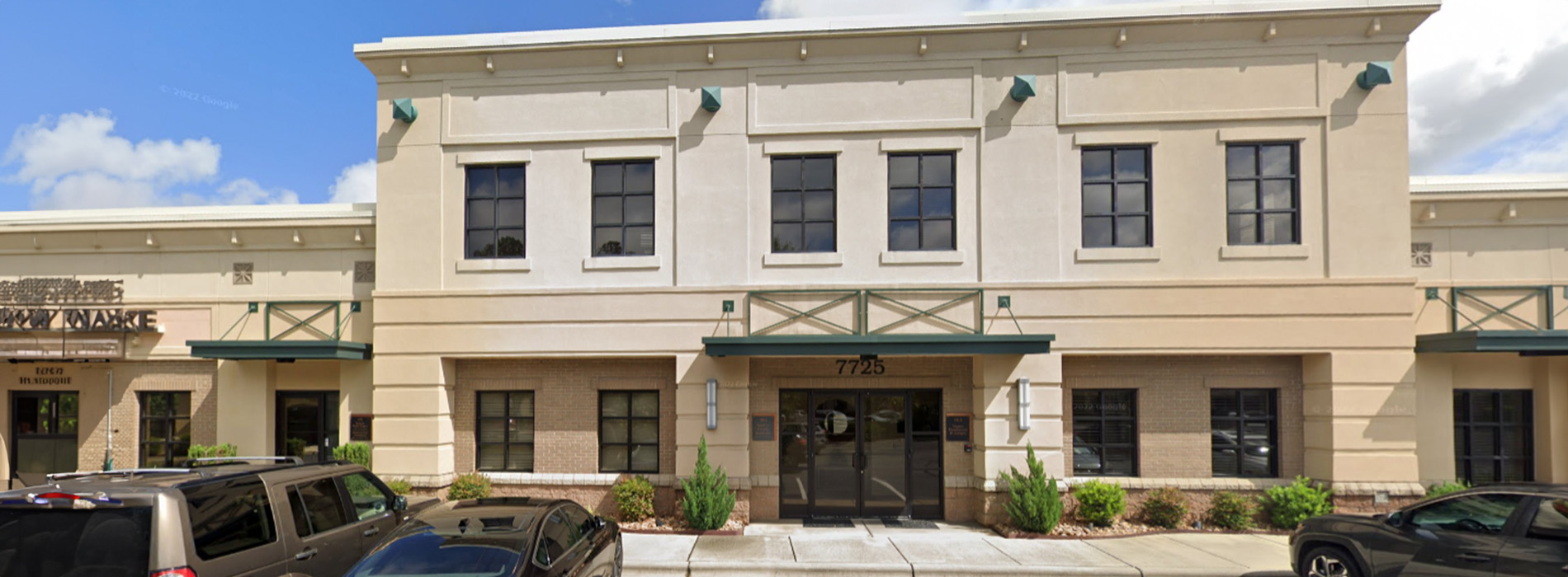 A building with a parking lot in the foreground, featuring two visible storefronts and a clear sky.