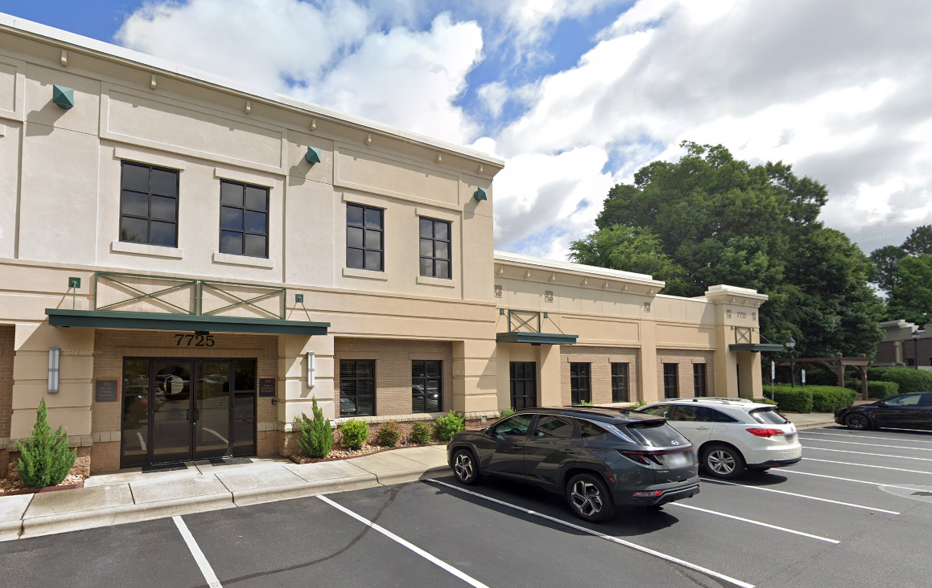 A two-story building with a cream facade, a flat roof, and a parking lot with several cars parked.