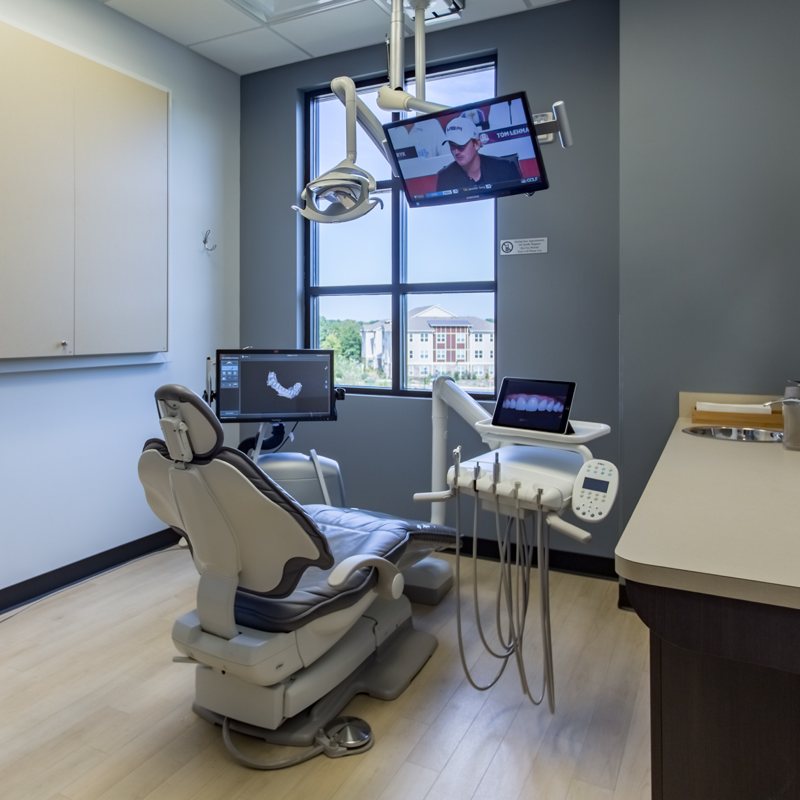 An interior view of a dental office with modern equipment, including a chair for patients and a computer screen displaying medical imagery.